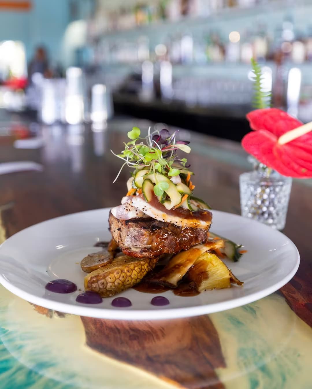A stacked filet plated over potatoes and topped with microgreens in an open-air Kona dining room