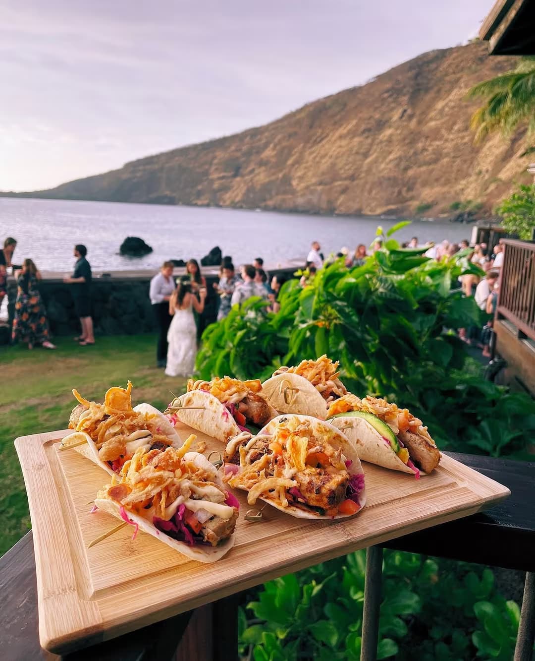 A wooden board of Baja fish tacos served oceanfront with Kealakekua Bay in the background