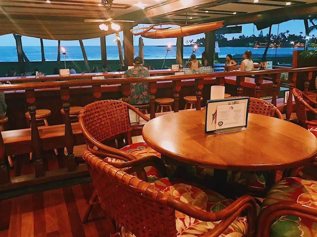The historic Kona Inn dining room with koa tables, rattan chairs, and open-air ocean views