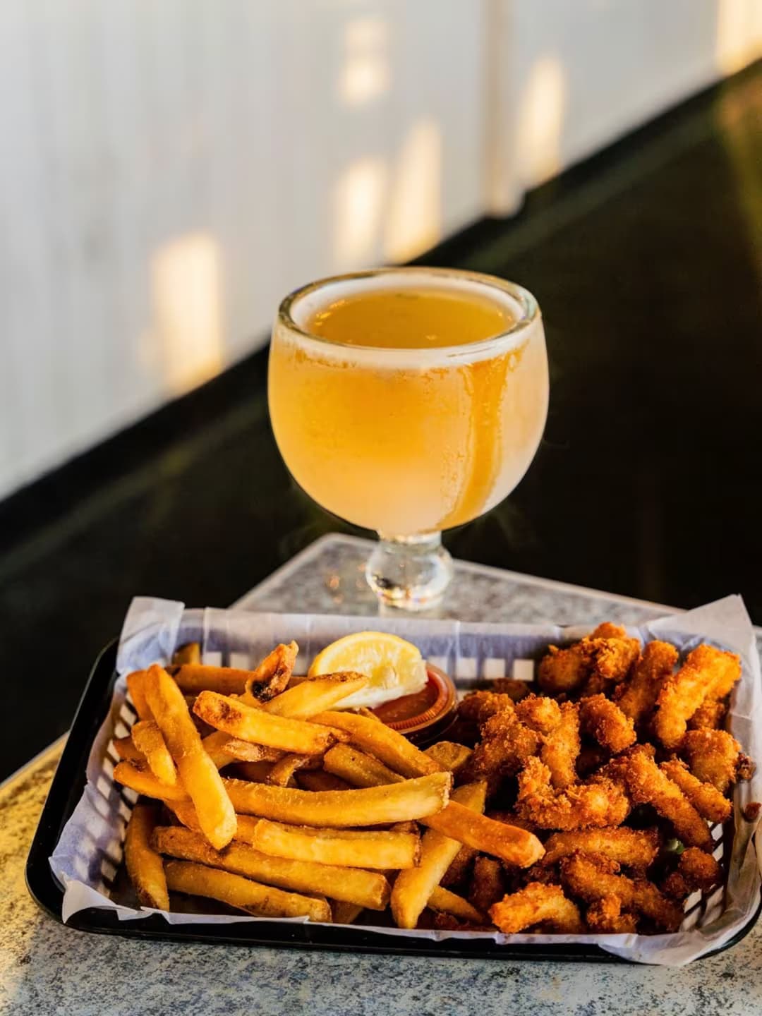 A Harbor House fried shrimp and fries basket next to an ice-cold golden beer at the harbor rail