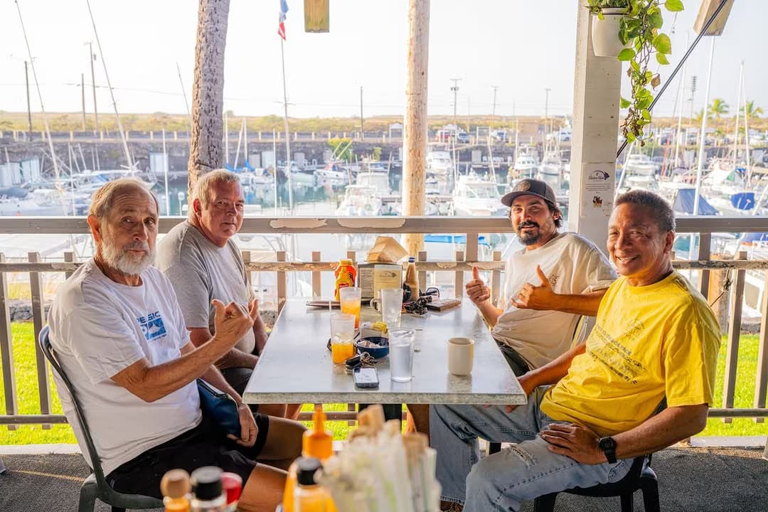 Four Kona regulars at a table by the Honokohau Harbor rail at golden hour